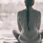 Woman in sweater looking outside at cold winter scene