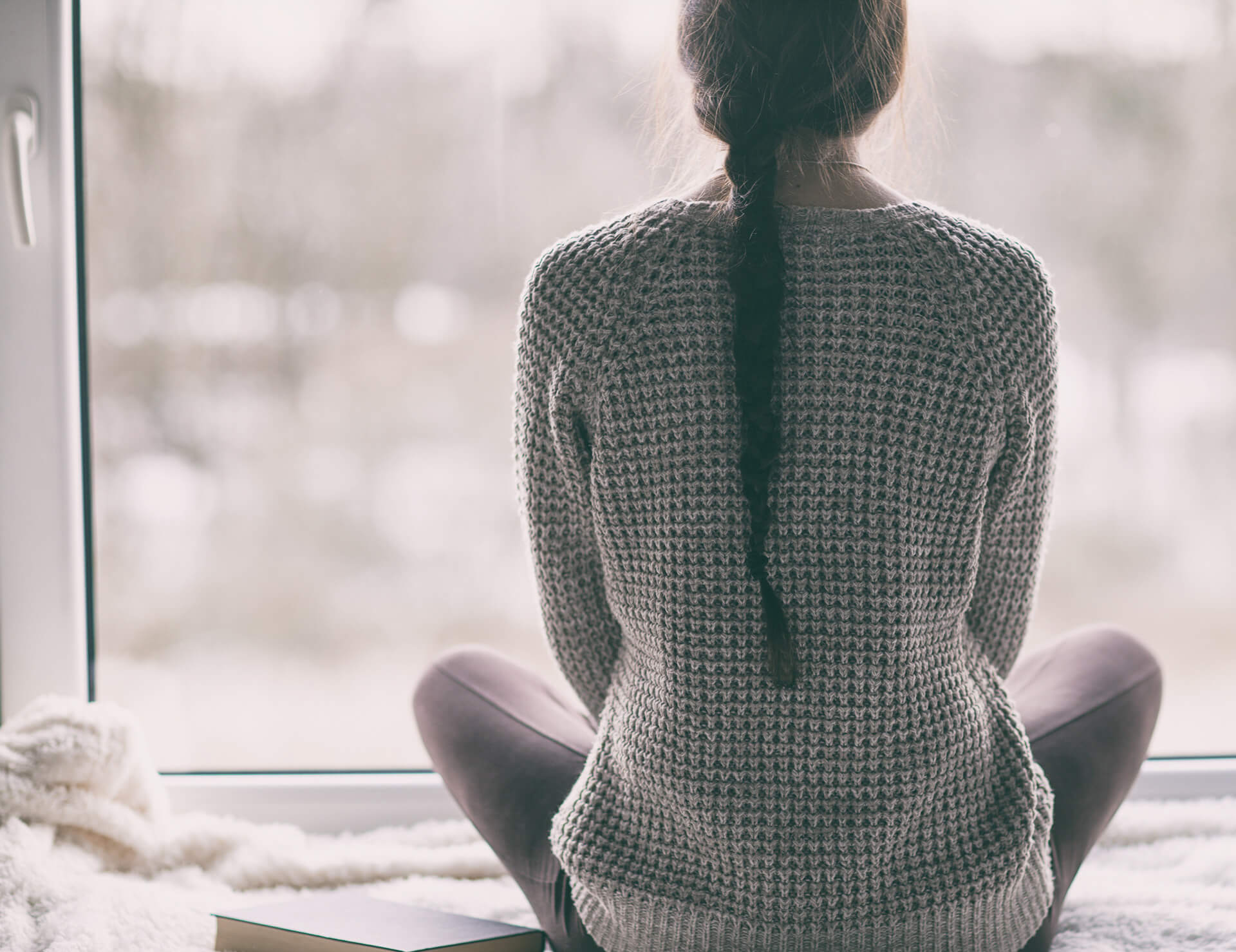 Woman in sweater looking outside at cold winter scene